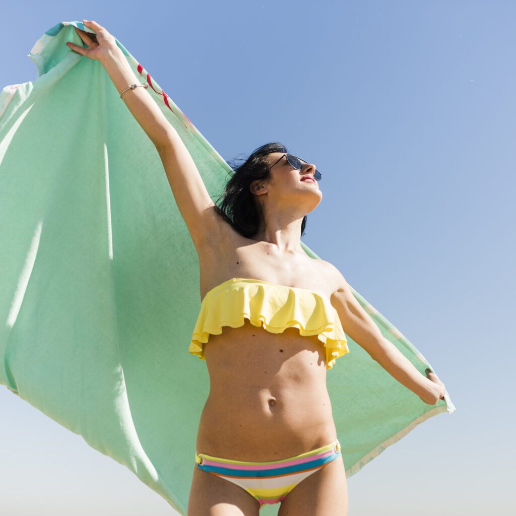 Mujer joven sujetando una toalla comn los brazos abiertos y cielo azul