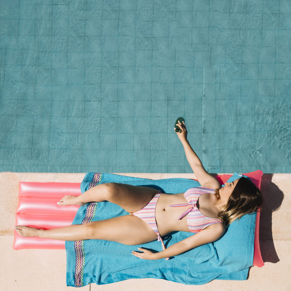 Mujer vista de arriba junto a piscina tomando el sol en toalla