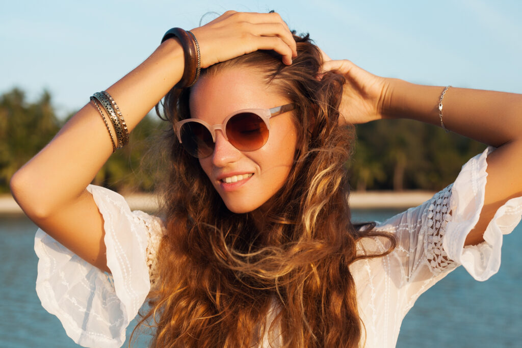 retrato de cerca de una hermosa mujer vestida de blanco en una playa tropical al atardecer con elegantes gafas de sol. chica de vacaciones, estilo verano. belleza natural, pelo largo, accesorios boho hippie