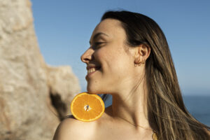 mujer sonriendo en la playa con naranja rica en vitamina C